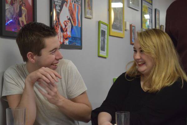 Conor and Laura are sat in the Students’ Union Bar at university. They are looking at one another and have been captured mid-laughter.